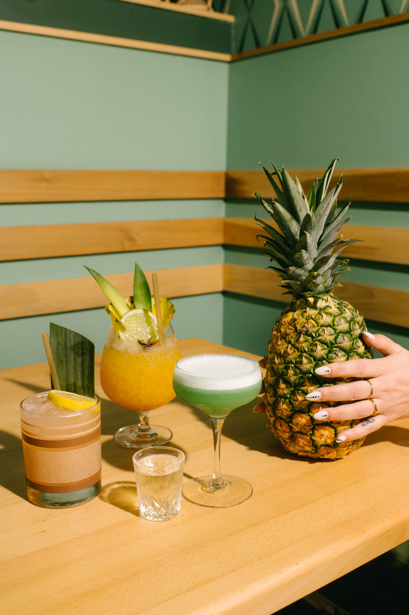 A pineapple style cocktail sitting on a wood tabletop in a green, lively booth